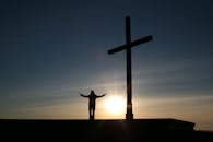 Silhouette of Person Standing Beside Cross during Sunset